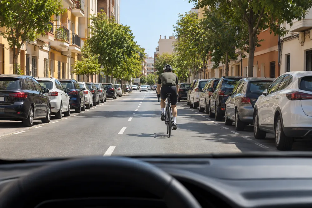 Ciclista circulando por el centro del carril en una calle urbana, delante de un turismo.