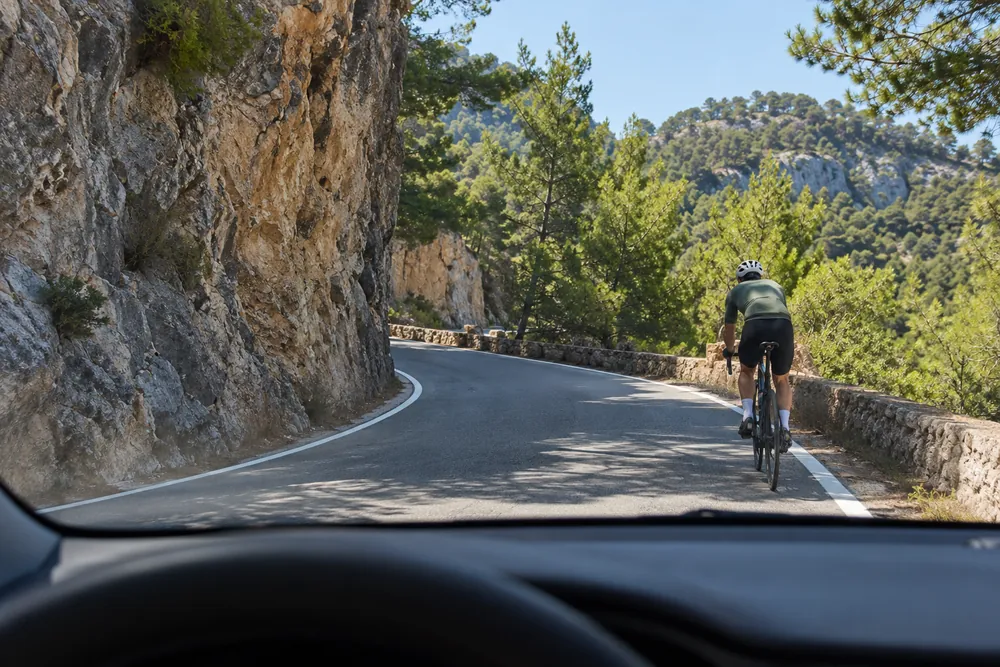 Ciclista circulando por una curva cerrada sin visibilidad de una carretera de montaña.