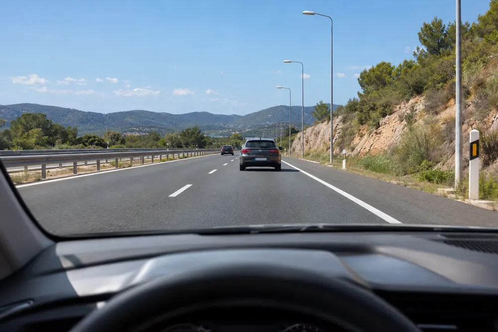 Turismo que sigue a otro por autovía con una farola como referencia para medir la distancia.